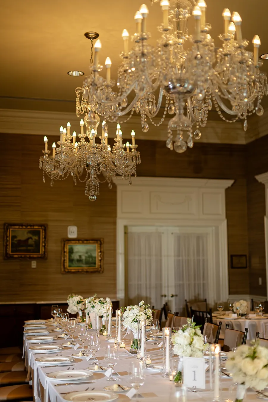 Crystal chandeliers over a long table of white roses and taper candles at Charlotte Country Club