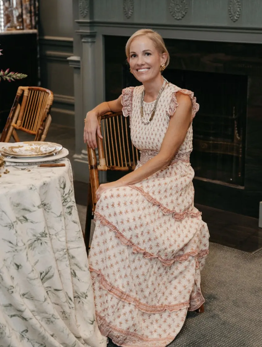 Ashley Snider smiling, seated on a bamboo chair beside a dressed table in a paneled dining room