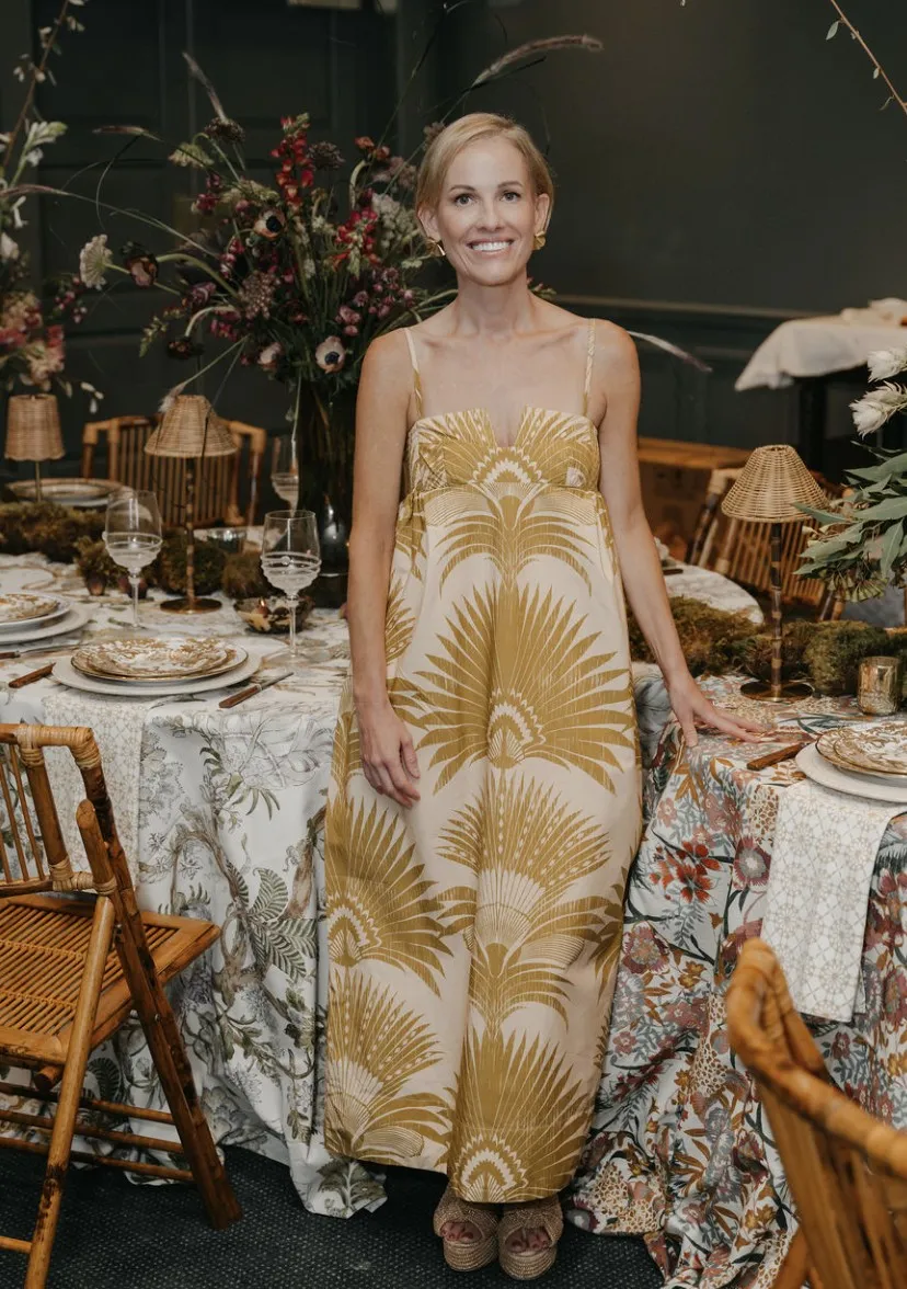 Ashley Snider standing beside a floral tablescape in a golden palm print dress