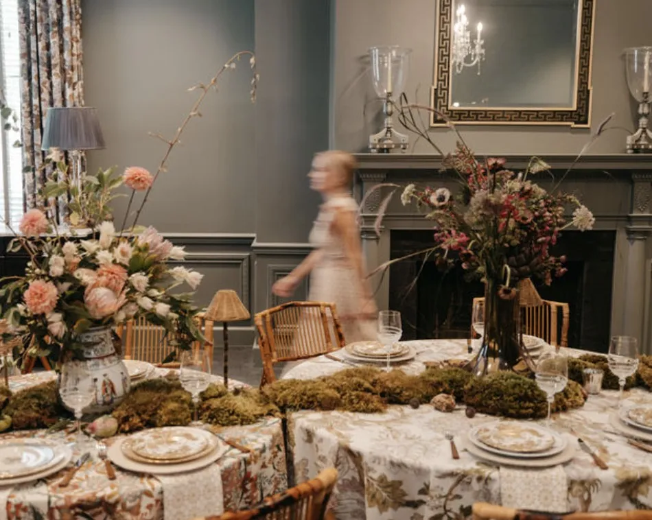 Ashley walking past a finished tablescape of moss runners, garden roses and patterned linens